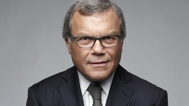 Ein Mann mit Brille und Anzug vor einem grauen Hintergrund.