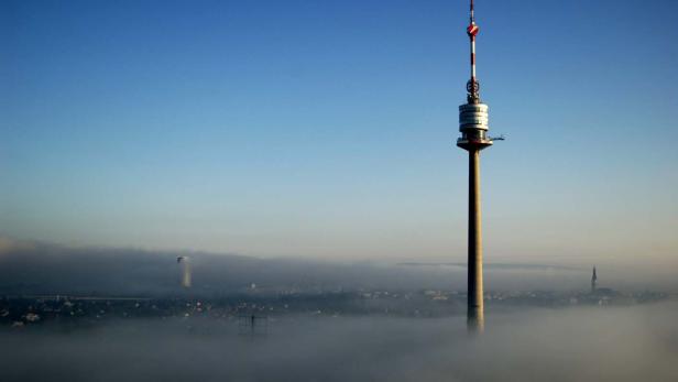 Der Donauturm ragt über eine nebelverhangene Stadtlandschaft hinaus.