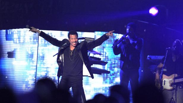 Lionel Richie tritt mit seiner Band auf einer Bühne auf.