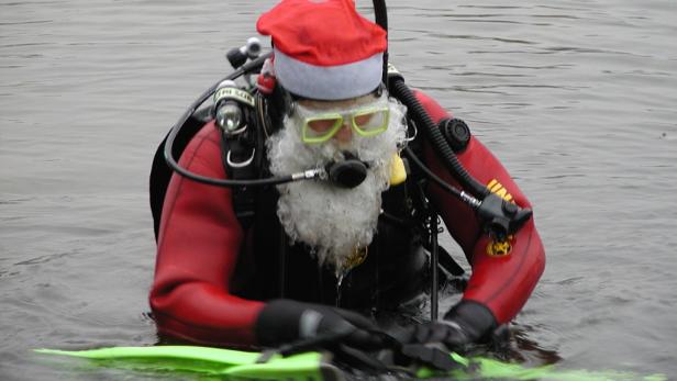 Ein Taucher mit Weihnachtsmannmütze und Bart steht im Wasser.