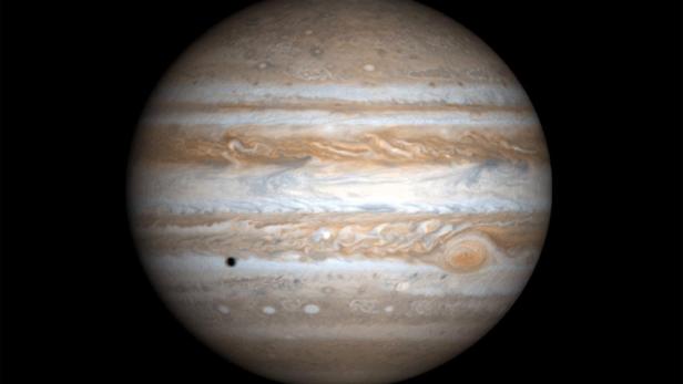 Der Planet Jupiter mit seinem großen roten Fleck und einem Jupitermond, der einen Schatten wirft.