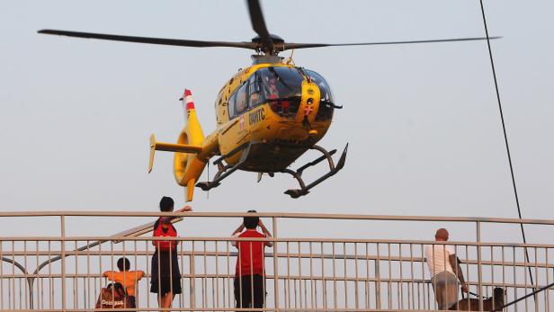 Ein gelber Rettungshubschrauber der ÖAMTC über einer Brücke mit Zuschauern.
