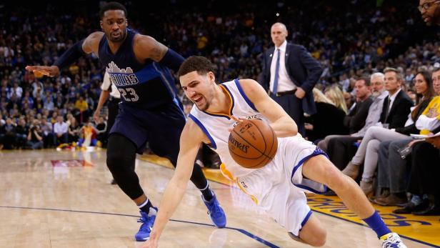 Ein Basketballspieler der Golden State Warriors dribbelt den Ball, während ein Verteidiger der Dallas Mavericks ihn verfolgt.