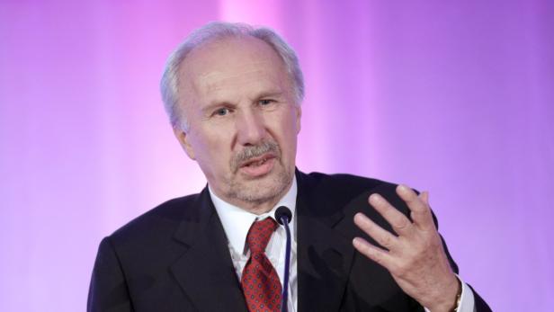 Ein Mann in einem dunklen Anzug und einer roten Krawatte spricht in ein Mikrofon.