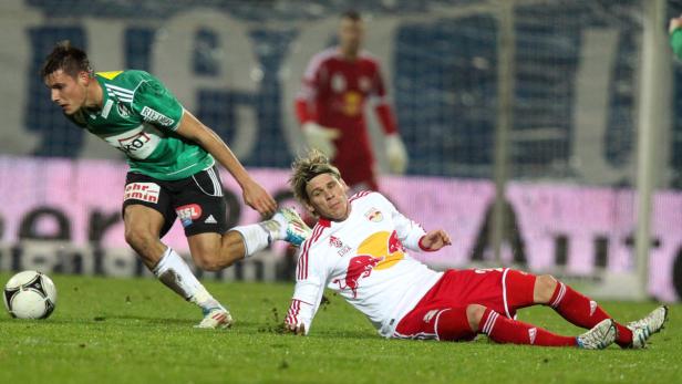 Ein Fußballspieler grätscht, während ein anderer versucht, den Ball zu erobern.