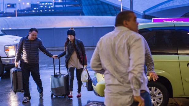 Zwei Reisende mit Gepäck verlassen ein Flughafengebäude, während ein Taxifahrer wartet.