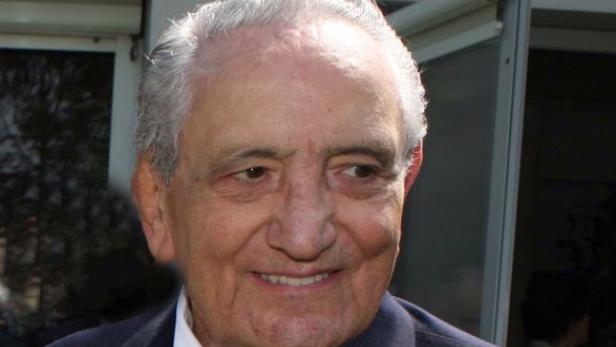 Ein lächelnder älterer Mann mit grauem Haar und einem dunklen Anzug.