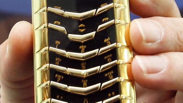 Nahaufnahme eines goldenen Mobiltelefons mit Tastenfeld, das von einer Hand gehalten wird.