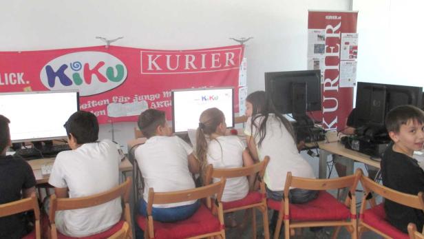 Kinder sitzen an Computern unter einem Banner von „Kiku“ und „Kurier“.