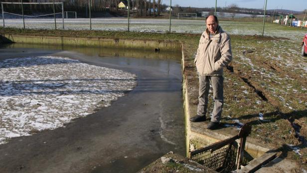Ein Mann steht an einem teilweise gefrorenen Teich in der Nähe eines Fußballfeldes.