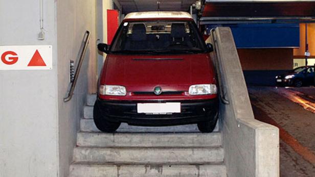 Ein rotes Auto steht auf einer Treppe vor einer Garage.