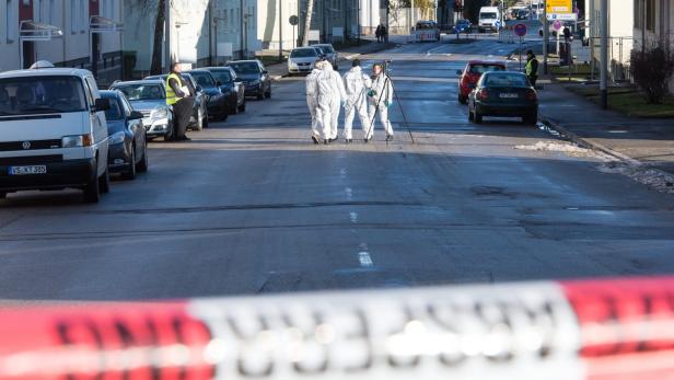 Polizisten in Schutzanzügen untersuchen einen Tatort auf einer abgesperrten Straße.