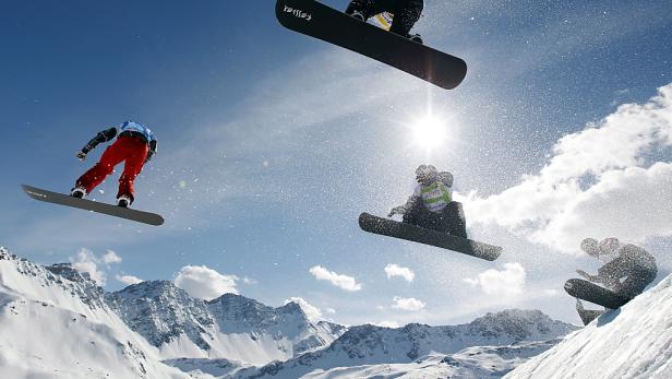 Mehrere Snowboarder springen vor einer Bergkulisse in der Luft.