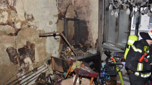 Ein Zimmer mit Brandschäden und ein Feuerwehrmann im Einsatz.