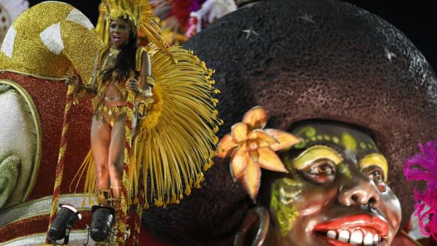 Eine Frau in einem goldenen Karnevalskostüm steht neben einer großen, bemalten Figur.