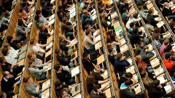 Ein voll besetzter Hörsaal mit Studierenden, die an ihren Tischen sitzen und lernen.