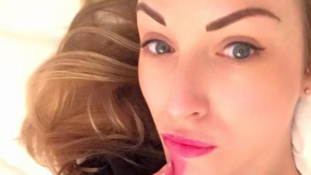 Eine Frau mit blonden Haaren und pinkfarbenem Lippenstift blickt in die Kamera.