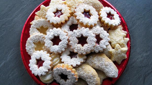 Ein roter Teller ist gefüllt mit verschiedenen Weihnachtsplätzchen, die mit Puderzucker bestäubt sind.