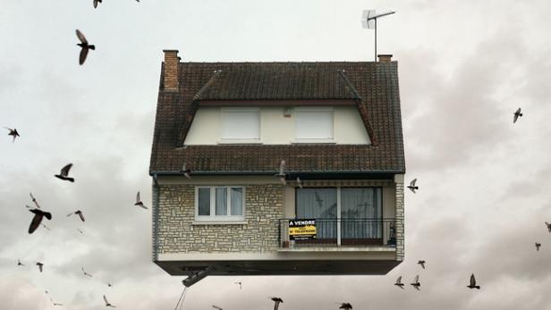 Ein Haus schwebt inmitten einer Wolke von Vögeln, ein „Zu Verkaufen“-Schild am Balkon.