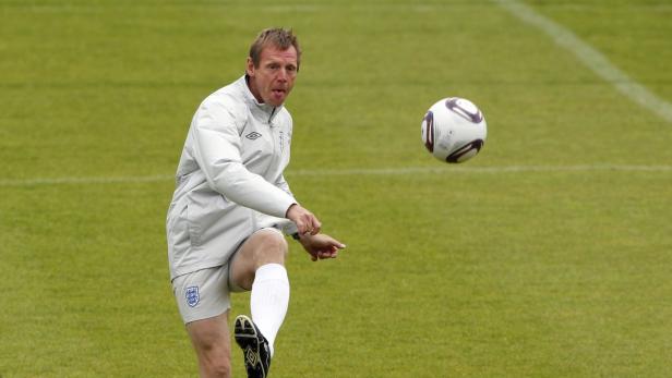 Ein Mann im Trainingsanzug jongliert einen Fußball auf einem grünen Rasen.