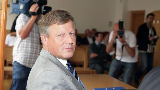 Ein Mann im Anzug blickt in die Kamera, umgeben von Kameraleuten und Fotografen.