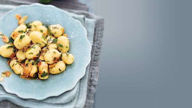 Gnocchi mit Mandeln und Kräutern auf einem hellblauen Teller angerichtet.