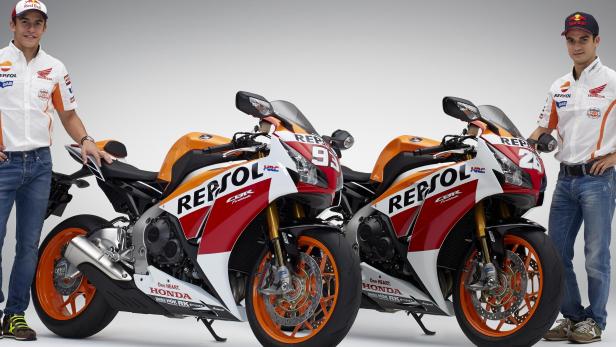 Zwei Rennfahrer posieren neben ihren Repsol Honda CBR Motorrädern.