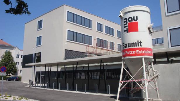 Ein Baumit Silo steht vor einem modernen Gebäude mit großen Fenstern.