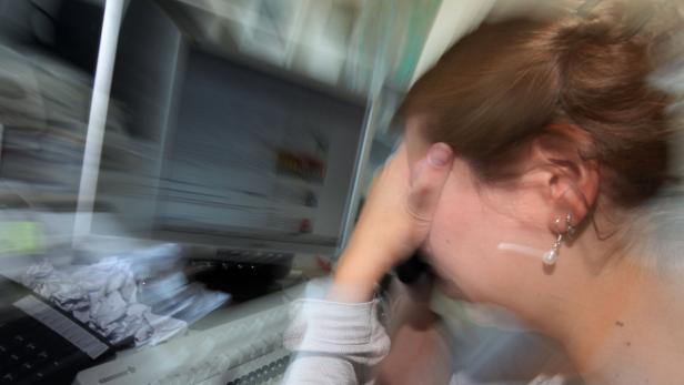 Eine Frau sitzt vor einem Computer und hält sich die Hand vor das Gesicht.