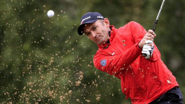 Ein Golfspieler im roten Hemd schlägt einen Golfball.
