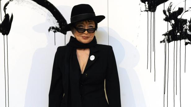 Yoko Ono posiert vor einem abstrakten Gemälde mit schwarzer Farbe.