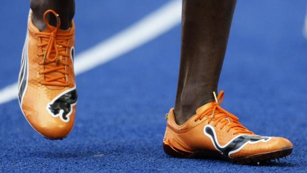 Nahaufnahme von orangefarbenen Puma-Spikes auf einer blauen Laufbahn.