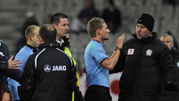 Ein Fußballtrainer diskutiert mit einem Schiedsrichter auf dem Spielfeld.