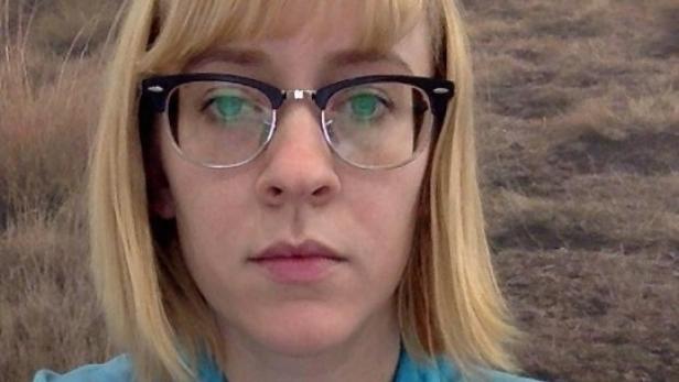 Eine Frau mit blonden Haaren und Brille blickt in die Kamera.