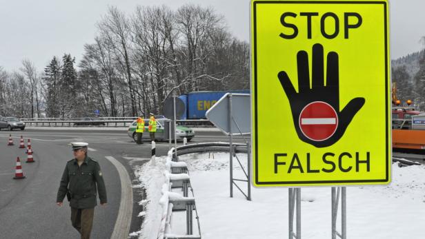 Ein gelbes Schild mit der Aufschrift „STOP FALSCH“ und einer Hand mit einem roten Kreis darauf steht an einer winterlichen Straße.