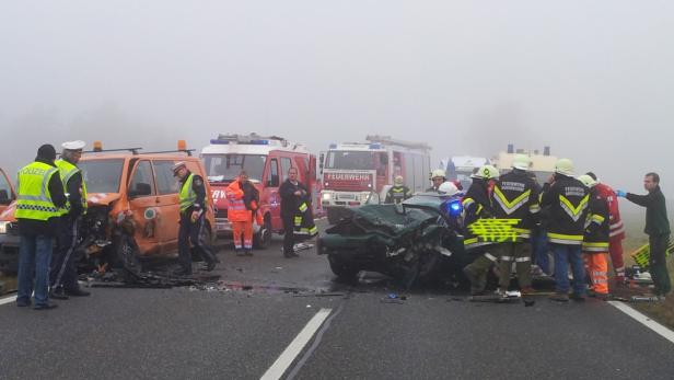 Auf einer nebligen Straße stehen beschädigte Fahrzeuge und Einsatzkräfte von Polizei, Feuerwehr und Rettungsdienst.