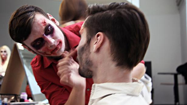 Ein Mann mit Zombie-Make-up berührt das Gesicht eines anderen Mannes.