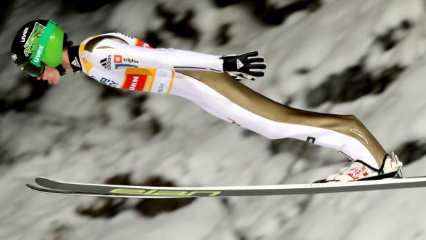 Ein Skispringer in der Luft vor einer verschneiten Landschaft.
