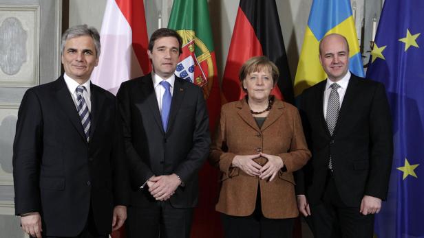 Angela Merkel posiert mit drei weiteren Politikern vor verschiedenen Nationalflaggen.