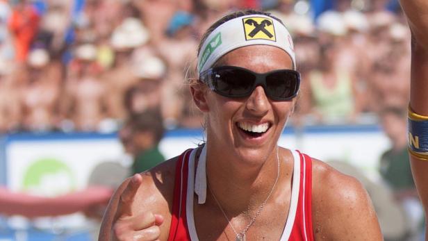 Eine lächelnde Beachvolleyballspielerin mit Sonnenbrille und Stirnband vor einer Zuschauermenge.