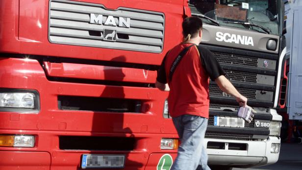 Ein Mann geht zwischen einem roten MAN-Lkw und einem grauen Scania-Lkw hindurch.