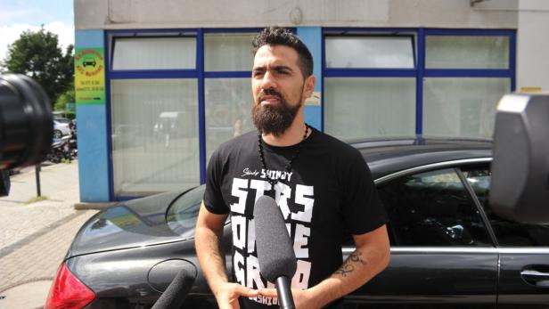 Bushido steht vor einem schwarzen Auto und spricht in ein Mikrofon.