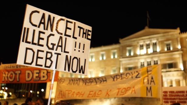 Demonstranten fordern den Erlass illegaler Schulden vor einem beleuchteten Gebäude.