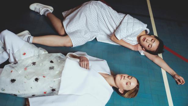 Zwei Frauen liegen in weißer Kleidung auf einem blauen Hallenboden.