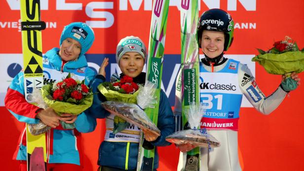 Drei Skispringerinnen stehen mit Blumensträußen auf dem Siegerpodest.