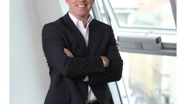 Ein Mann mit Brille und Anzug steht vor einem Fenster.