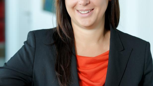 Eine lächelnde Frau in einem schwarzen Blazer und einem roten Oberteil.