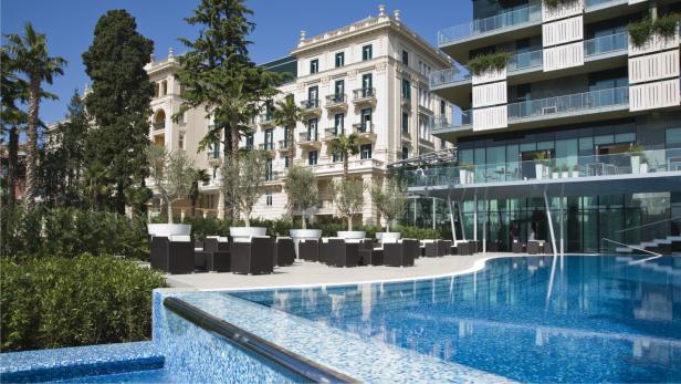 Ein Schwimmbad vor einem Hotelgebäude mit Palmen und Sitzgelegenheiten.