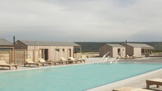 Ein Schwimmbad mit hellblauem Wasser und mehreren Holzhäusern im Hintergrund.