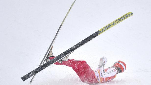 Ein Skispringer stürzt im Schnee, die Skier ragen in die Luft.
